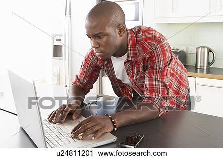 Stock Image - Young Man Using Laptop In Modern Kitchen . Fotosearch