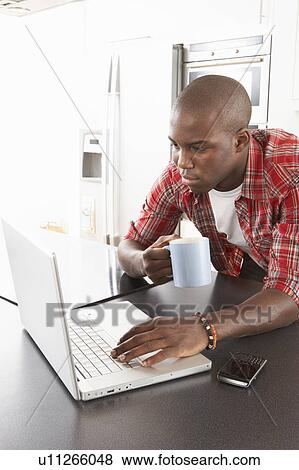 Stock Photo - Young Man Using Laptop In Modern Kitchen . Fotosearch