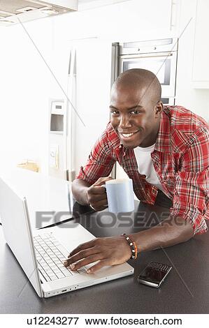 Stock Photo - Young Man Using Laptop In Modern Kitchen . Fotosearch