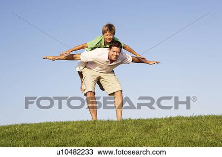 Stock Image - Young man with boy playing in a field. Fotosearch