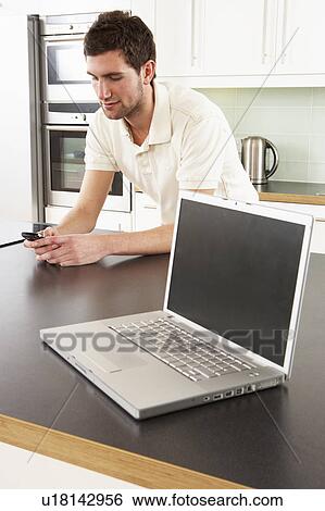 Stock Photograph - Young Man With Laptop In Modern Kitchen . Fotosearch