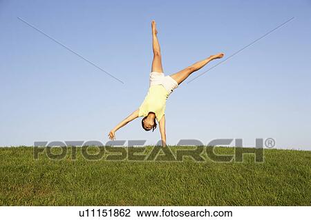 Stock Image - Young woman cartwheels in field. Fotosearch