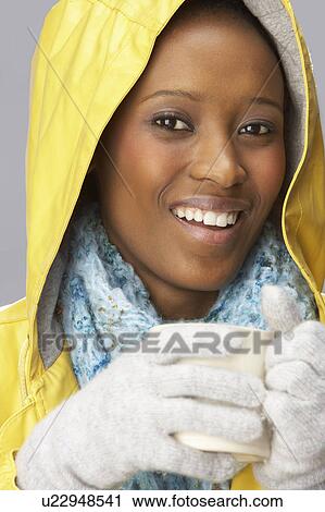 Stock Image - Young Woman Drinking Hot Drink Wearing Yellow Raincaot. Fotosearch