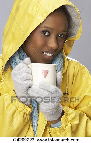 Stock Image - Young Woman Drinking Hot Drink Wearing Yellow Raincaot. Fotosearch
