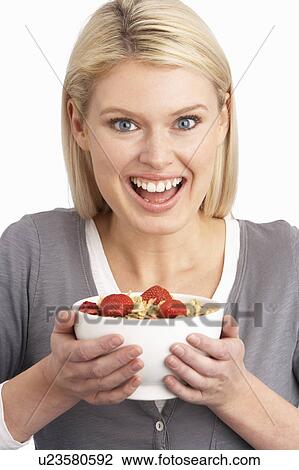 Stock Image - Young Woman Eating Bowl Of Healthy Breakfast Cereal In Studio. Fotosearch