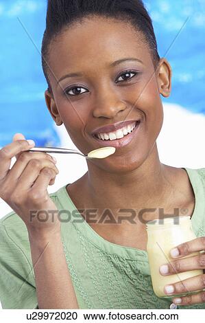 Stock Image - Young Woman Eating Yoghurt In Studio. Fotosearch