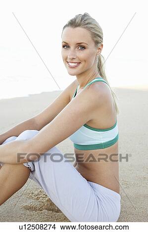 Picture - Young Woman In Fitness Clothing Resting After Exercise On Beach. Fotosearch