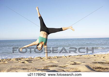 Stock Image - Young Woman In Fitness Clothing Turning Cartwheel On Beach. Fotosearch