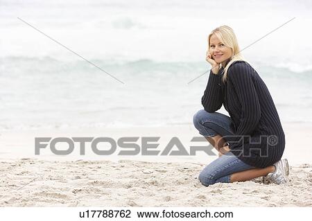 Stock Image - Young Woman On Holiday Kneeling On Winter Beach. Fotosearch
