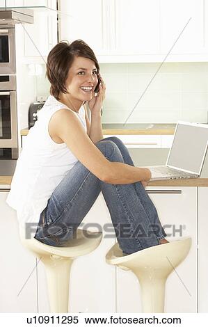 Stock Photography - Young Woman Relaxing Sitting In Kitchen Talking On Phone. Fotosearch