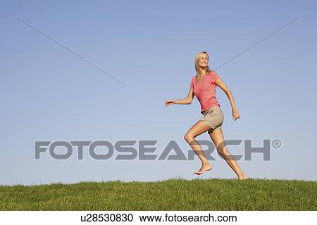 Young woman running through field View Large Photo Image Stock Image - Young woman running through field. Fotosearch