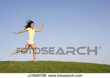 Young woman running through field View Large Photo Image Stock Photograph - Young woman running through field. Fotosearch