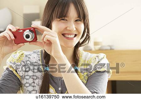Stock Image - Young Woman Taking Photograph On Digital Camera At Home . Fotosearch