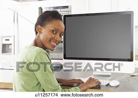 Picture - Young Woman Using Computer In Modern Kitchen . Fotosearch