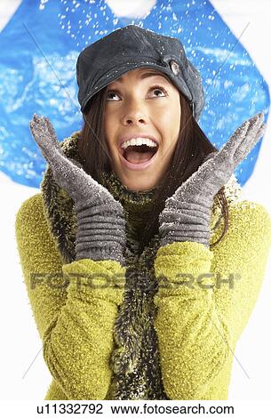 Stock Image - Young Woman Wearing Warm Winter Clothes And Hat Throwing Snowball In Studio. Fotosearch