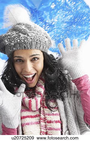 Stock Photo - Young Woman Wearing Warm Winter Clothes And Hat Being Hit By Snowball In Studio. Fotosearch