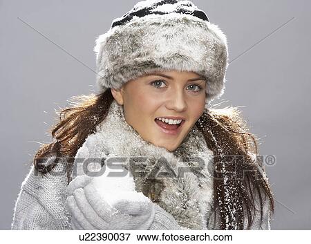 Stock Photo - Young Woman Wearing Warm Winter Clothes And Fur Hat Holding Snowball In Studio. Fotosearch