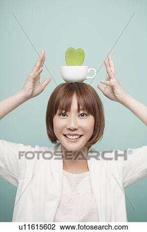 Stock Image - A woman holding a plant on her head. Fotosearch