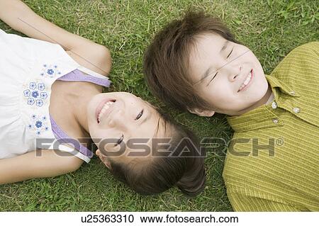 Stock Image - Boy and girl lying on grass, Chiba Prefecture, Honshu, Japan. Fotosearch