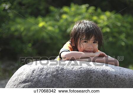Stock Image - Boy lying down on a rock, Niigata Prefecture, Honshu, Japan. Fotosearch