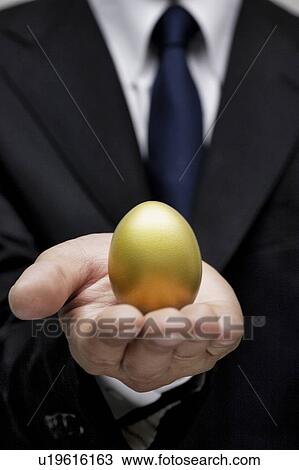 Stock Image - Businessman holding a golden egg. Fotosearch