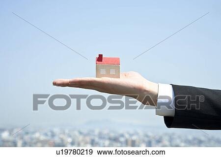 Stock Photo - Businessman holding a small house in his hand. Fotosearch