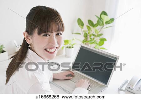 Stock Photo - Businesswoman looking at camera using a laptop. Fotosearch