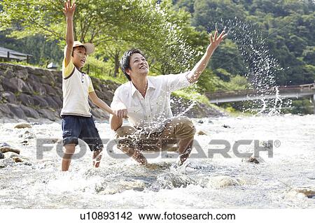 Stock Image - Father and Son Splashing Water in River. Fotosearch