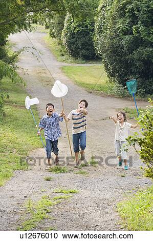 Stock Image - Kids running with butterfly nets to catch insects, Chiba Prefecture, Honshu, Japan. Fotosearch