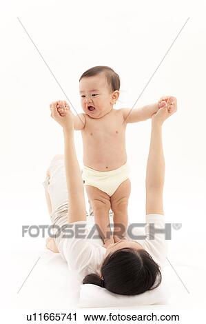 Stock Image - Mother Supporting Baby Boy to Stand on Her Chest. Fotosearch