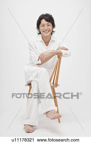 Stock Image - Portrait of young man sitting on chair. Fotosearch