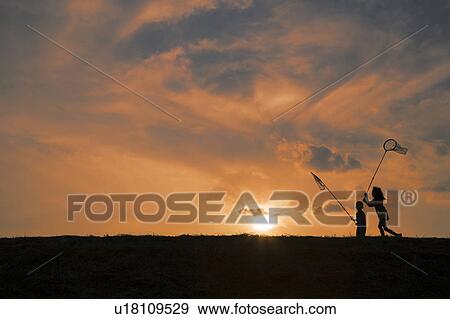 Stock Photo - Two Children Catching Insects at Sunset. Fotosearch