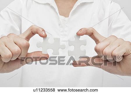 Stock Photo - Young man holding jigsaw pieces. Fotosearch