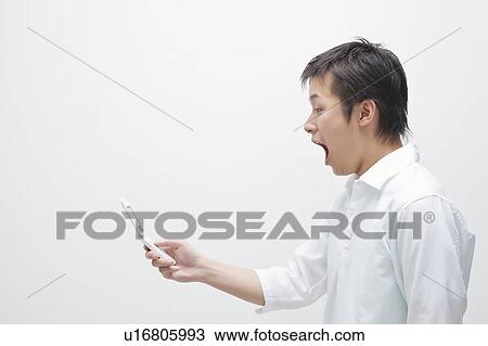 Young man looking at cell phone and shouting View Large Photo Image Stock Image - Young man looking at cell phone and shouting. Fotosearch