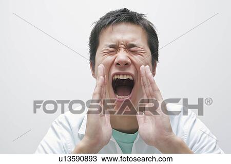 Stock Image - Young man shouting with hands covering mouth. Fotosearch