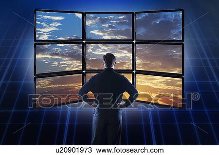 Stock Image - Businessman observing clouds on computer monitors. Fotosearch