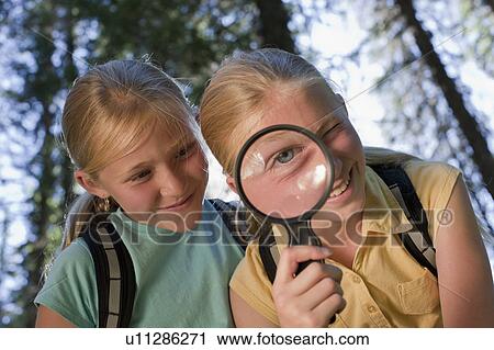 Stock Image - Canada, British Columbia, Fernie, sisters looking through magnifying glass. Fotosearch