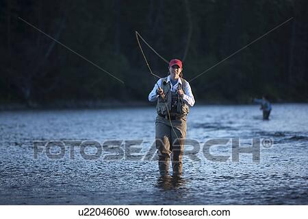 Stock Image - Canada, British Columbia, Fernie, Portrait of woman fly fishing in river. Fotosearch