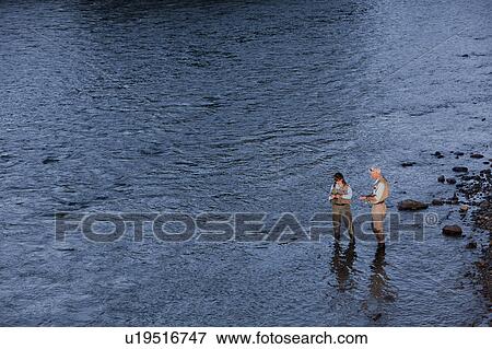 Stock Photo - Canada, British Columbia, Fernie, Couple fly fishing in river. Fotosearch