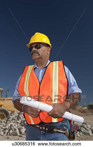 Stock Photograph - Construction worker holding blueprint on building site. Fotosearch
