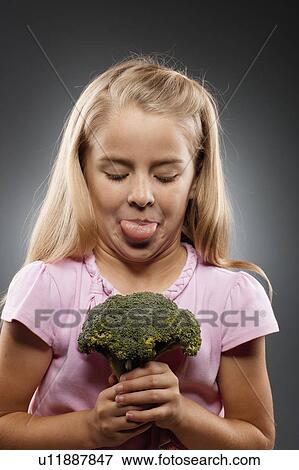Stock Photo - Girl (8-9) holding broccoli and sticking out tongue, studio shot. Fotosearch
