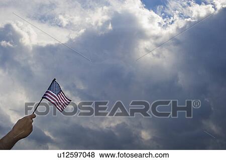 Hand holding American flag against cloudy sky View Large Photo Image Stock Photo - Hand holding American flag against cloudy sky. Fotosearch