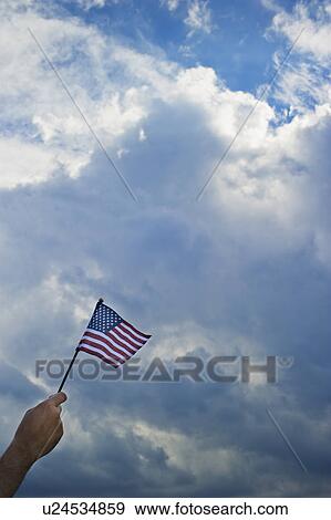 Hand holding American flag against cloudy sky View Large Photo Image Stock Photo - Hand holding American flag against cloudy sky. Fotosearch