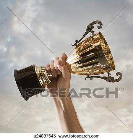 Stock Photography - Hand holding trophy against sky. Fotosearch