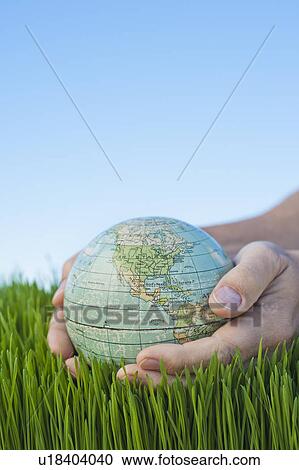 Stock Image - Male hands holding globe over grass. Fotosearch