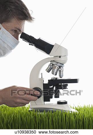 Stock Image - Man looking through microscope in studio. Fotosearch
