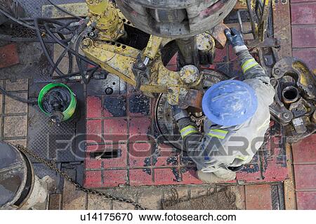Stock Image - Oil worker drilling for oil on rig. Fotosearch