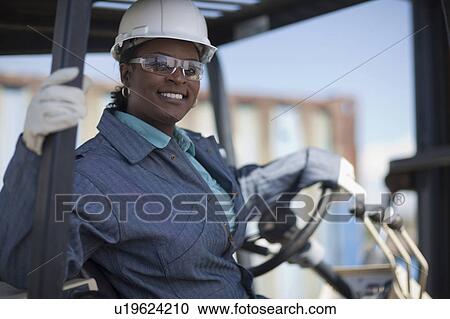 Stock Image - Portrait of female construction worker driving mechanical digger. Fotosearch