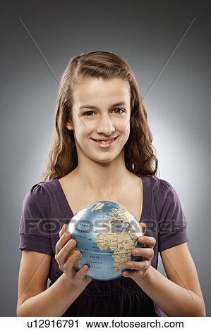Stock Image - Portrait of girl (12-13) holding globe and looking at camera, studio shot. Fotosearch