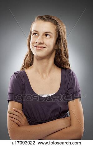 Stock Image - Portrait of girl (12-13) looking at camera with arms crossed, studio shot. Fotosearch